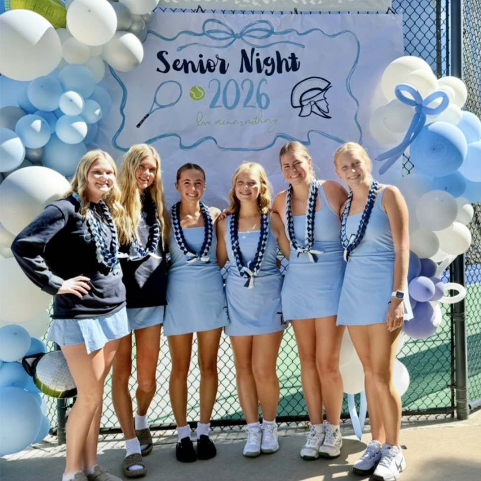 senior girls tennis players in front of a senior night sign and balloons