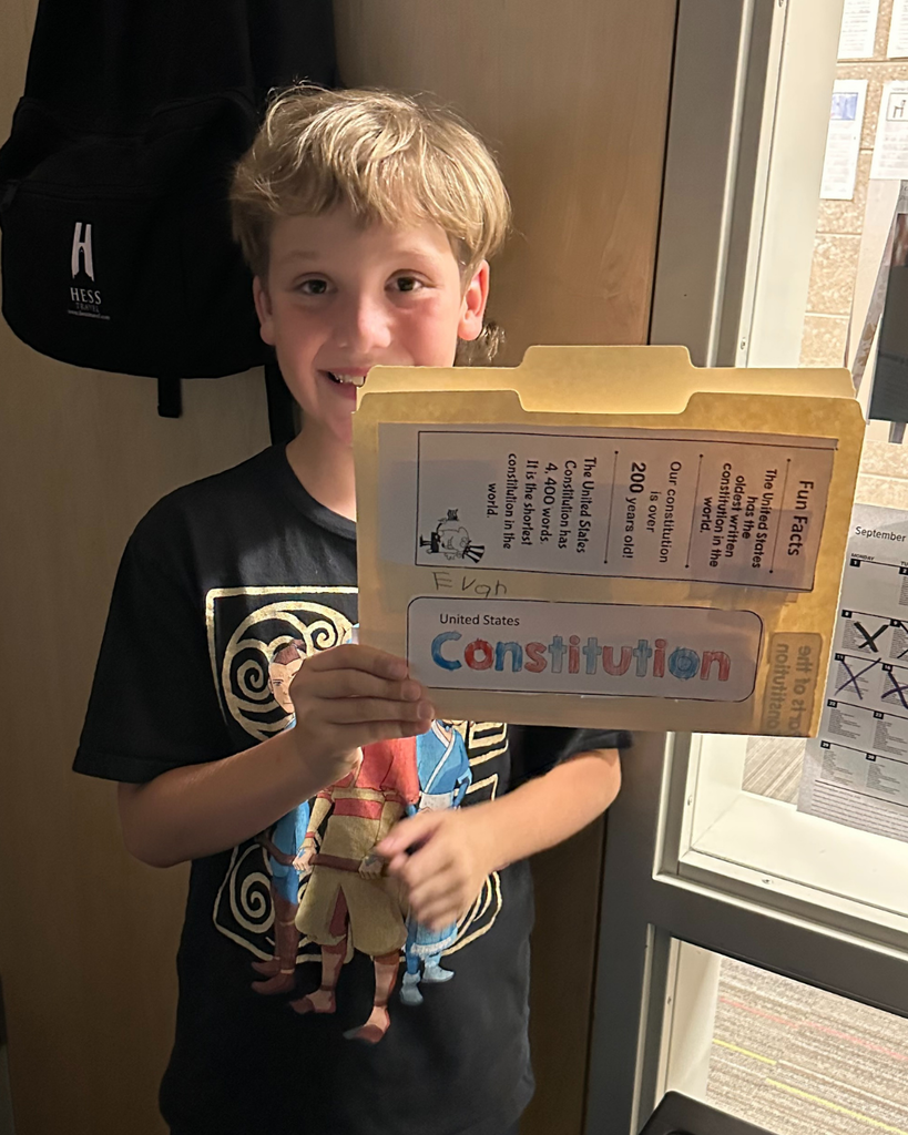 A student smiling as they hold up their Constitution folder. 