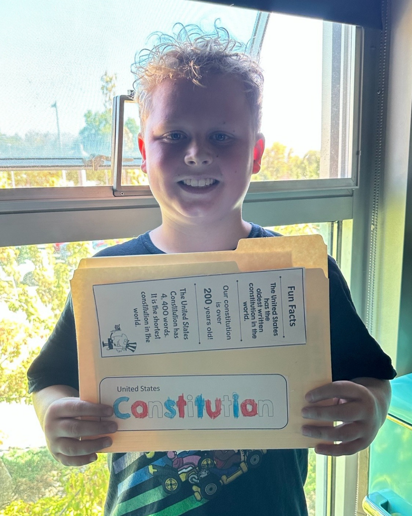 A student smiling as they hold up their Constitution folder. 