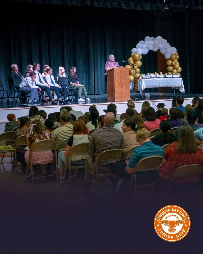 A speaker on stage in front of a group of parents and students in the school gym. 