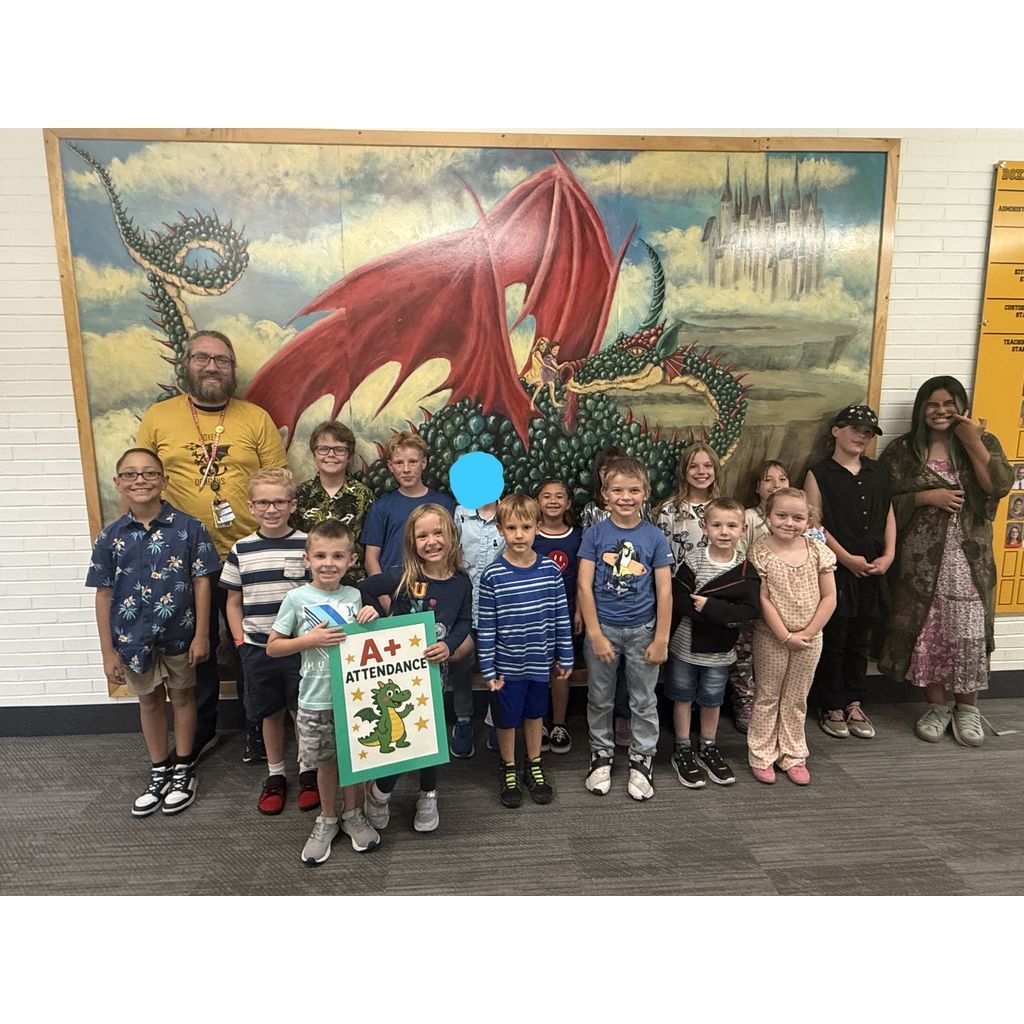 Doxey Elementary students and staff pose for a photo celebrating A+ Attendance in front of the school's dragon mural. One student is holding a green sign that says "A+ Attendance" with a dragon illustration.
