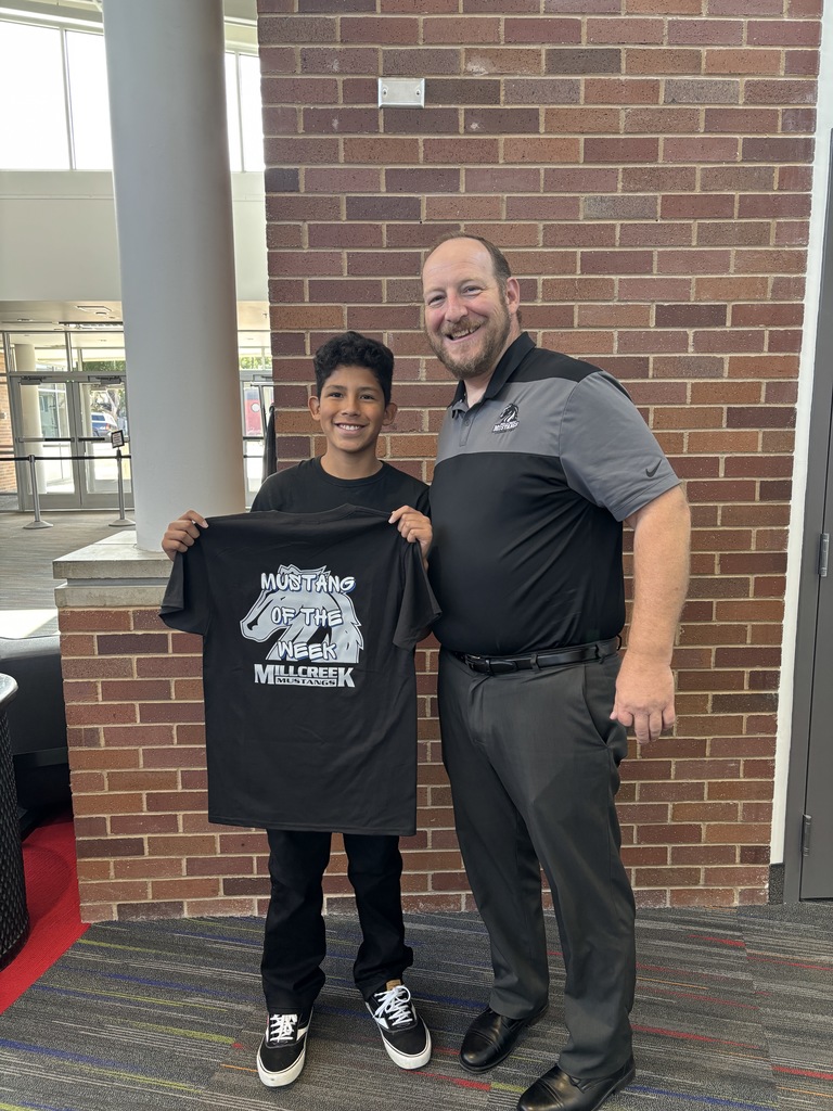 The Mustang of the Week standing beside the principal. Student is holding up his Mustang of the Week shirt