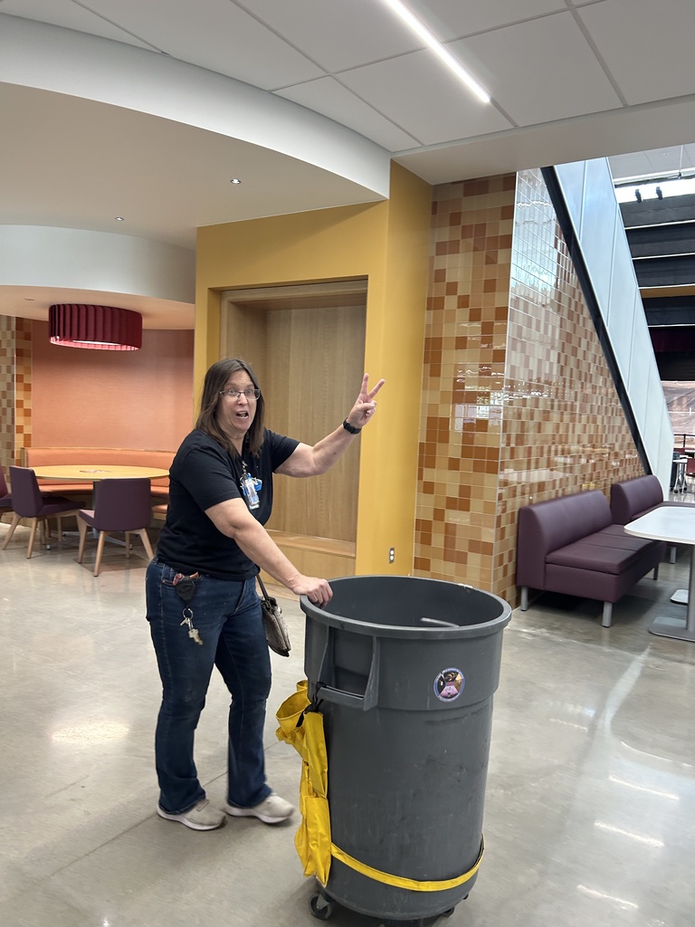 Mrs. Swank pushing a trash can in the hallway.