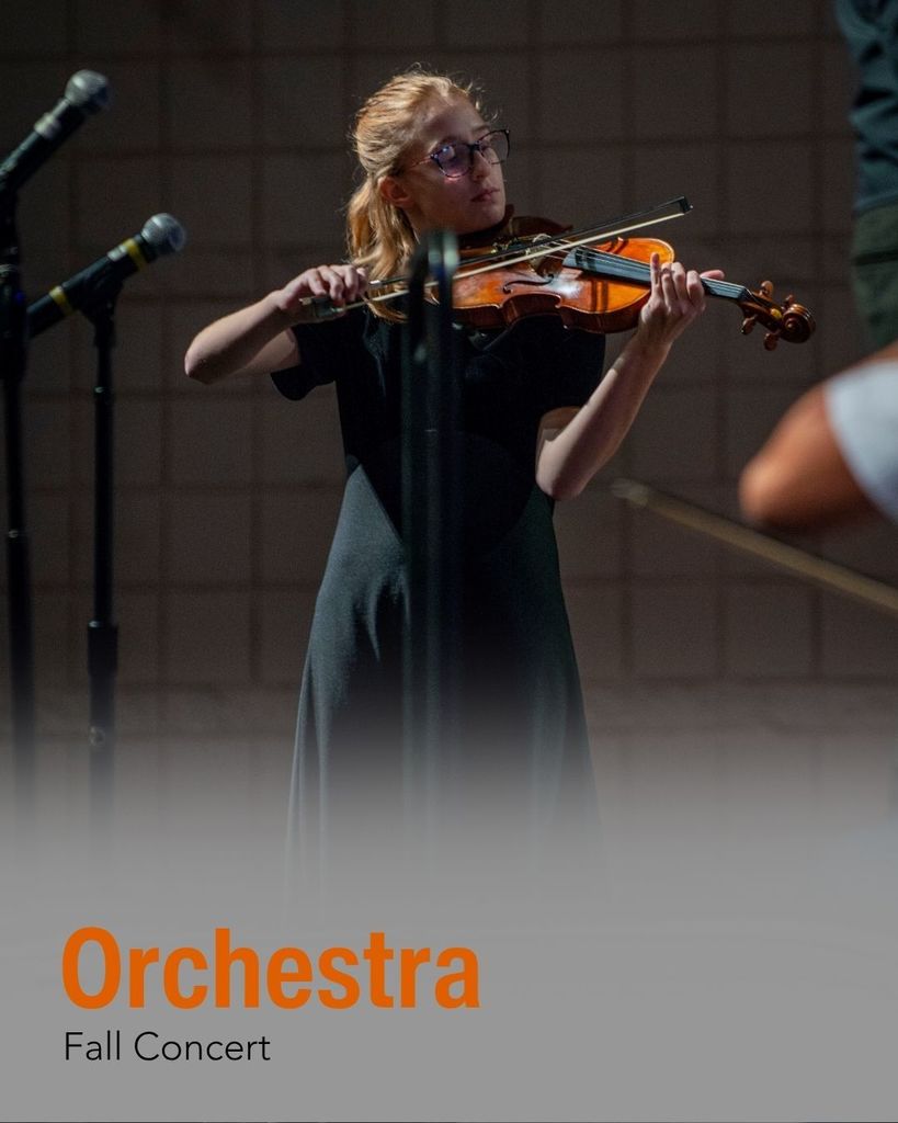 A soloist violin student stands on stage playing for her school's orchestra