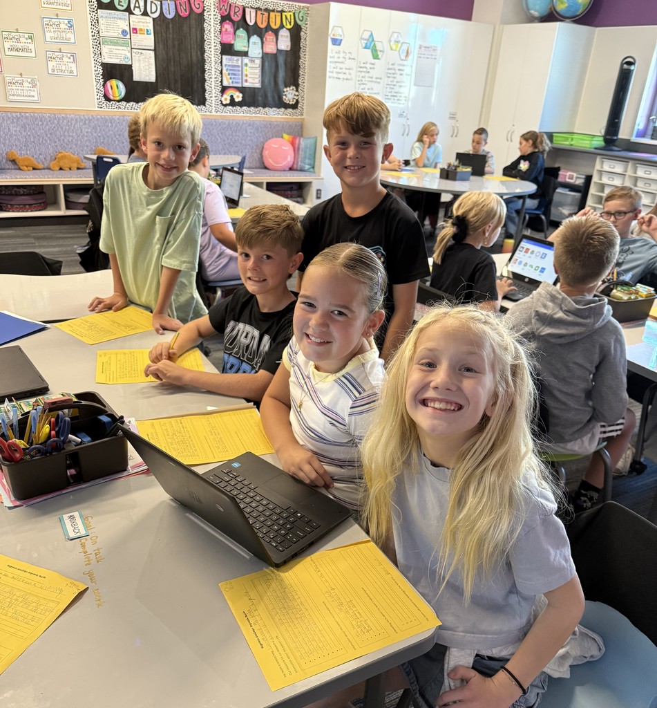 five students smiling with a laptop in front of them