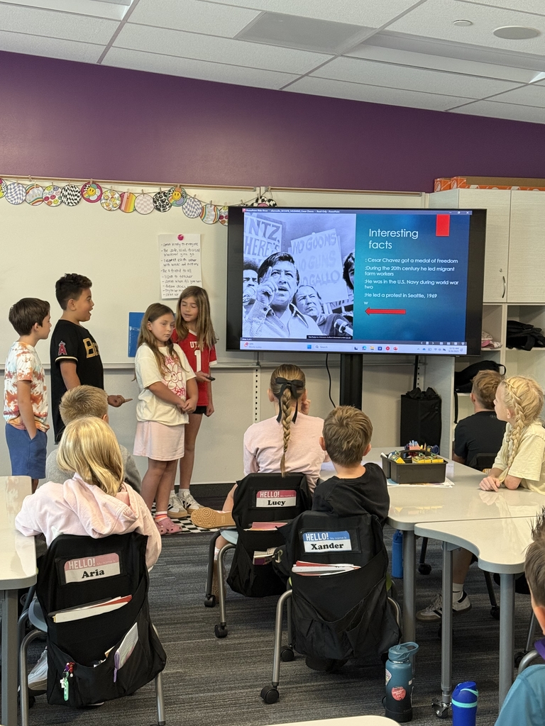 four students presenting in the front of their classroom with photo of man on tv