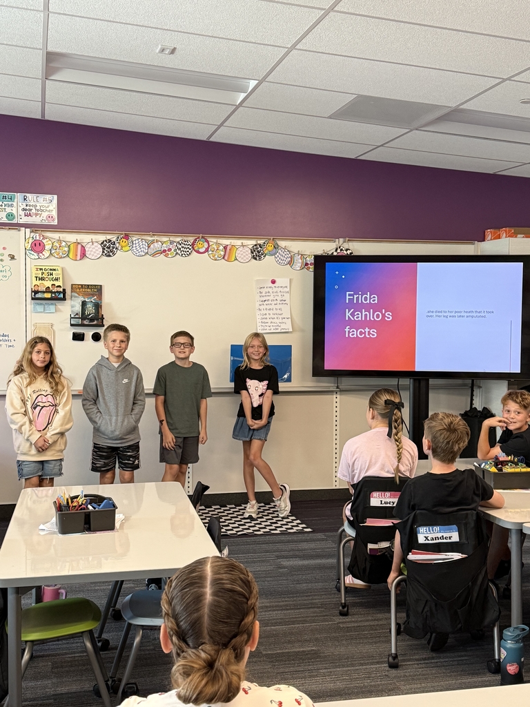Four students standing in the front of a classroom with presentation on Frida Kahlo's facts