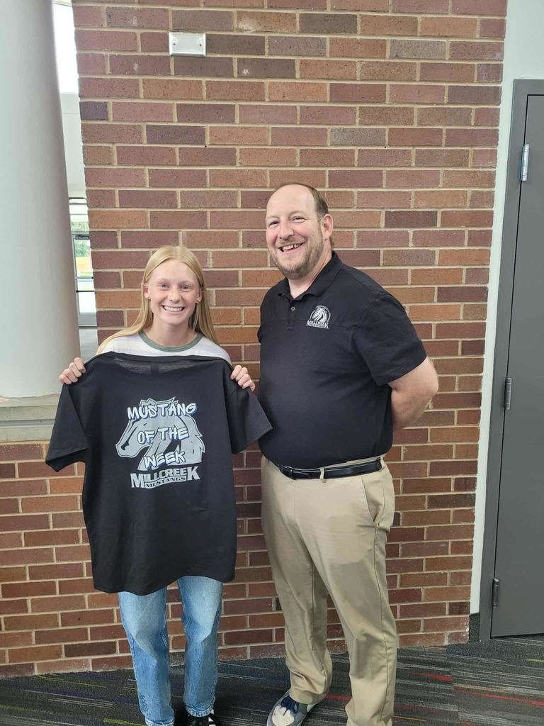 Pricipal Hansen with our Mustang of the Week. Student is holding up a black shirt with the Millcreek Mustang logo  with the letters over the logo that say "Mustang of the Week"