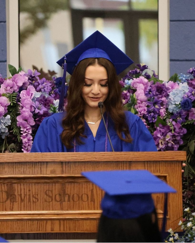 a Mountain High graduate speaking at a pulpit with flowers behind her.