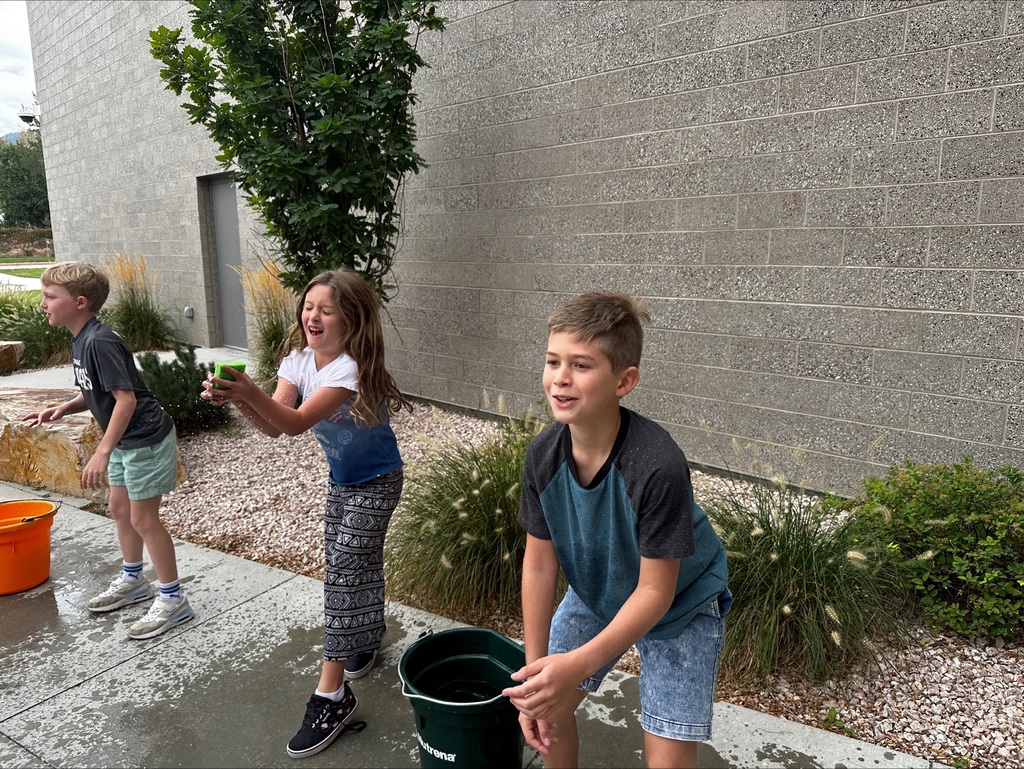 Two students standing next to a water bucket, catching sponges.