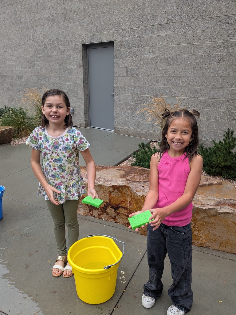 Two students holding sponges next to a water bucket