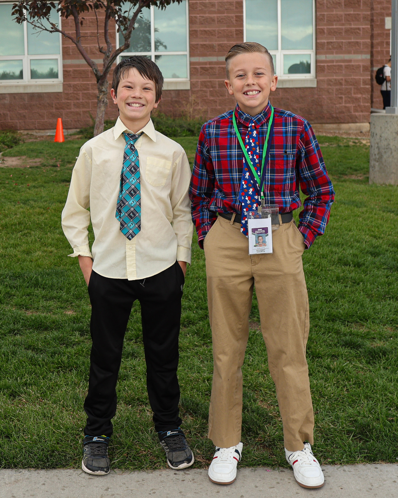 Two students standing wearing ties and button down shirts smiling.