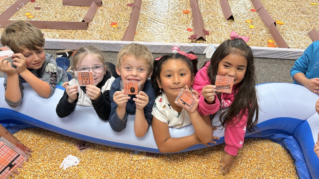 young students holding a coding card in front of a swimming pool of corn kernals