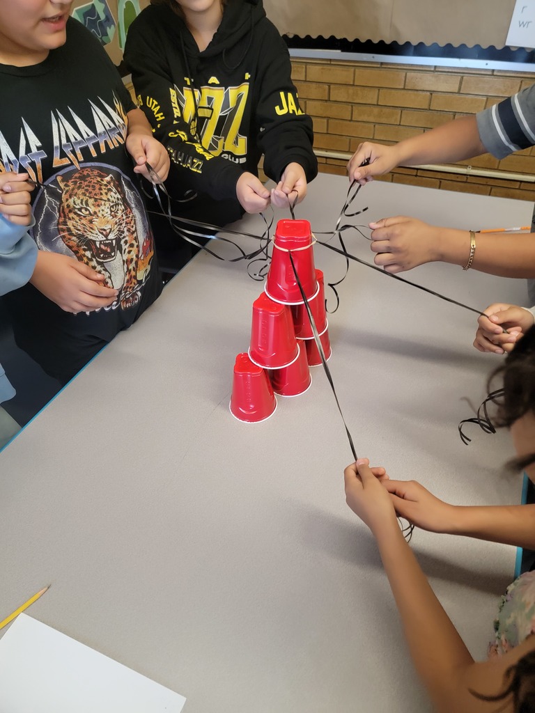 multiple students work together to stack cups in the shape of a pyramid