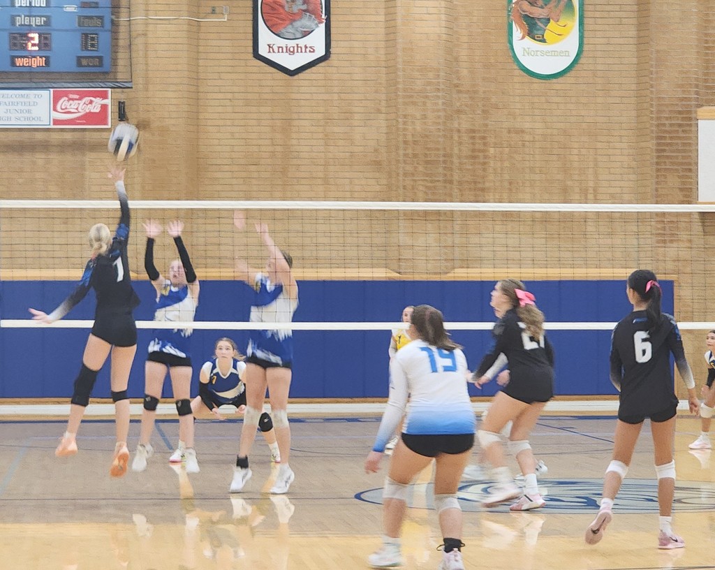 Fairfield's #7 is jumping to kill the ball against 2 Centerville players jumping for a block.  Other players are standing around, ready to dig the hit.