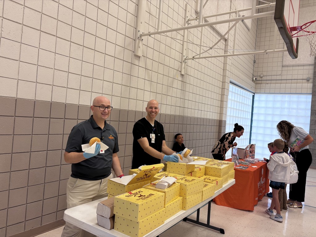 Two smiling men serving doughnuts to students