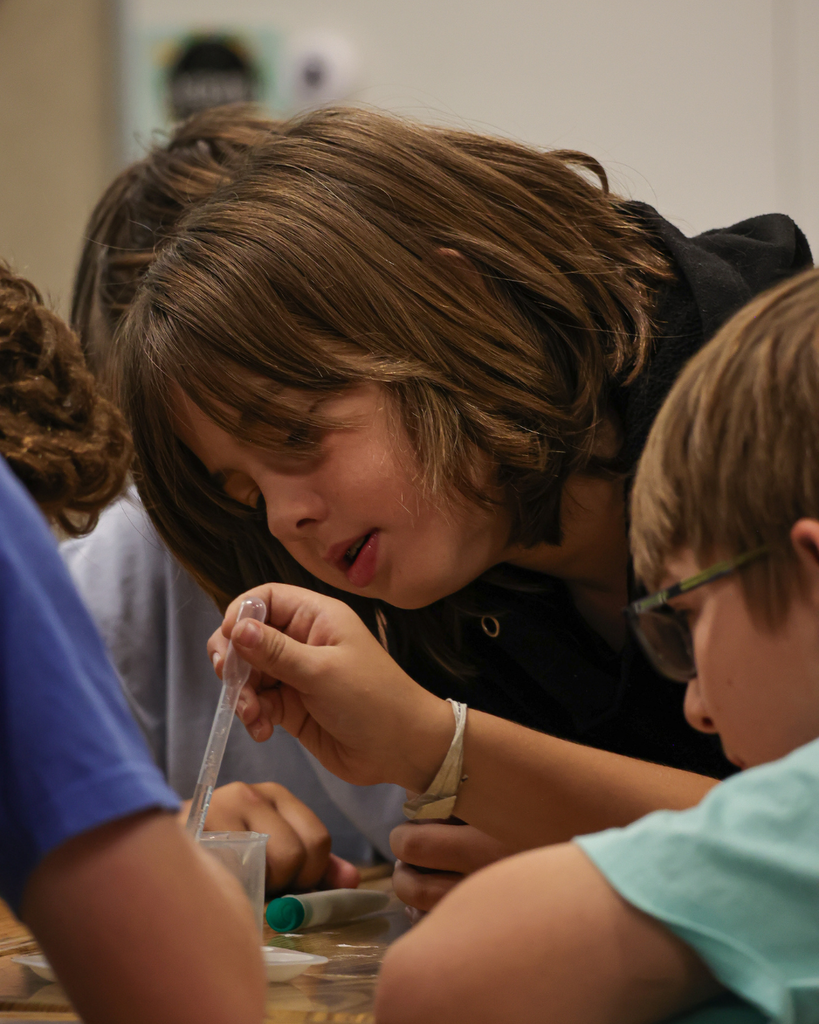 A student using a pipet to pull liquid from a beaker.