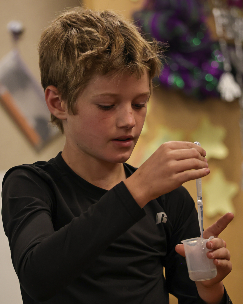 A student using a pipet to pull liquid from a beaker.