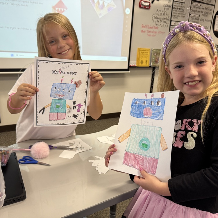 two girls holding up crayon pictures of matching monsters