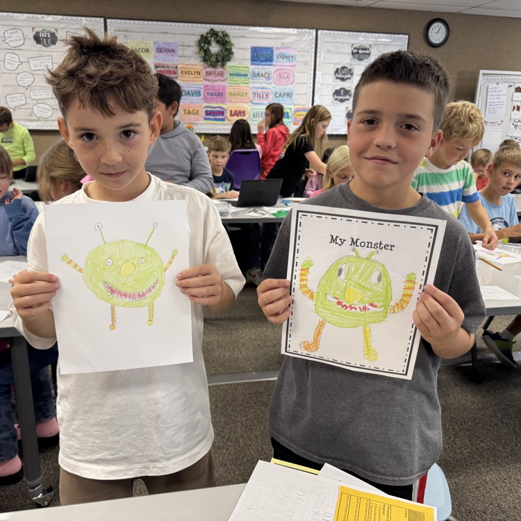 two boys holding up drawn pictures of a green monster