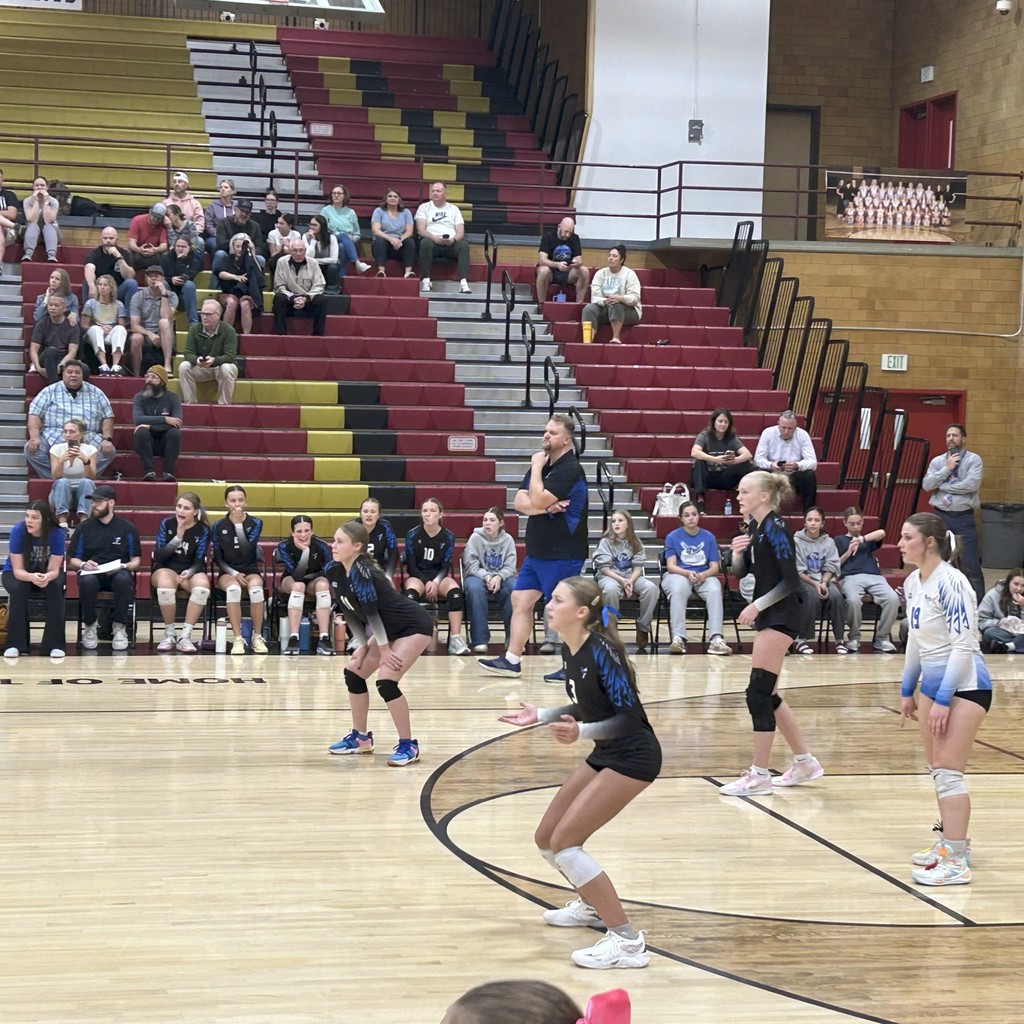 Fairfield's volleyball team ready for Horizon's serve.  The team bench is towards the back, with crowd members in the bleachers behind.