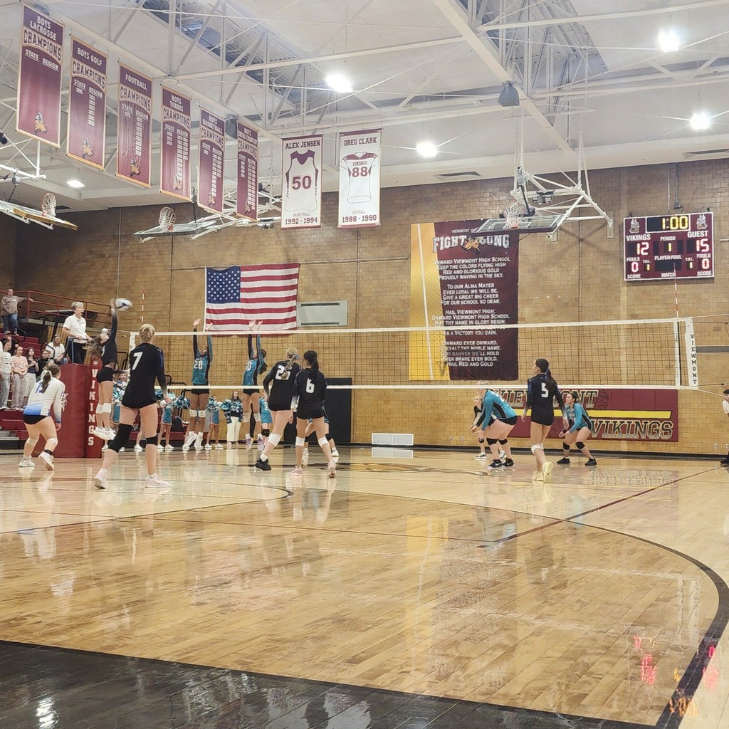 After an amazing set, Fairfield's hitter is attacking the ball.  Fairfield's team is on the near side of the net, Horizon has two blockers jumping, and the rest of their team is preparing for the hit.