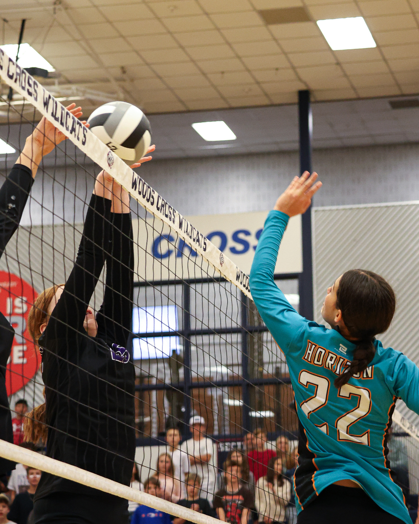 Two Centennial Junior High volleyball players guard the net as a Horizon player spikes the ball.