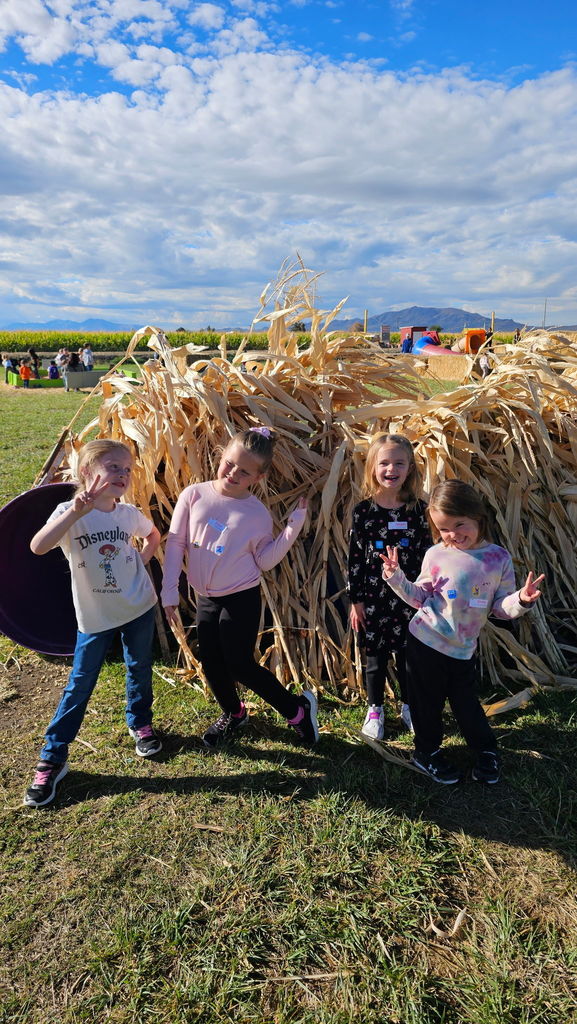 4young girls posing for the camera showing peace signs in front of corn stalks