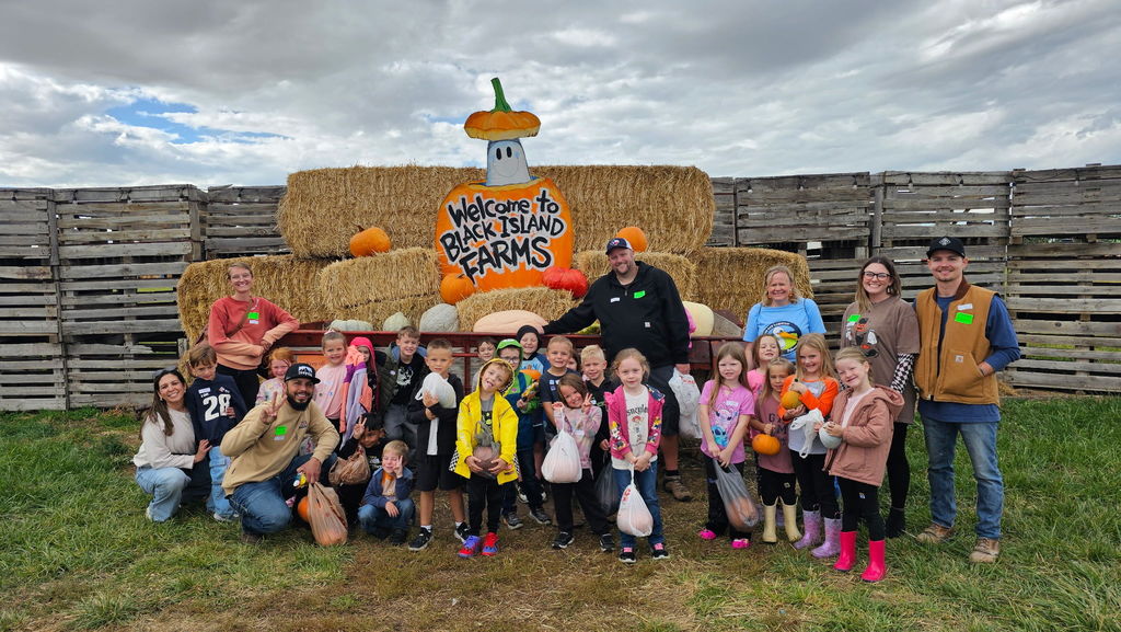 a class of students with parent chaperones posing in front of the Welcome to Black Island Farms signs