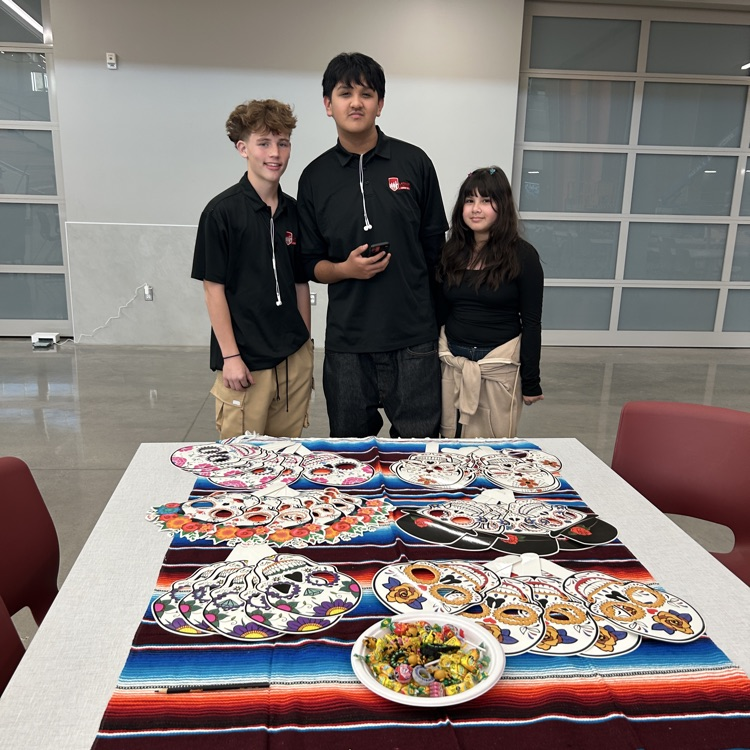 Three students stand behind a table with a colorful cloth and candy