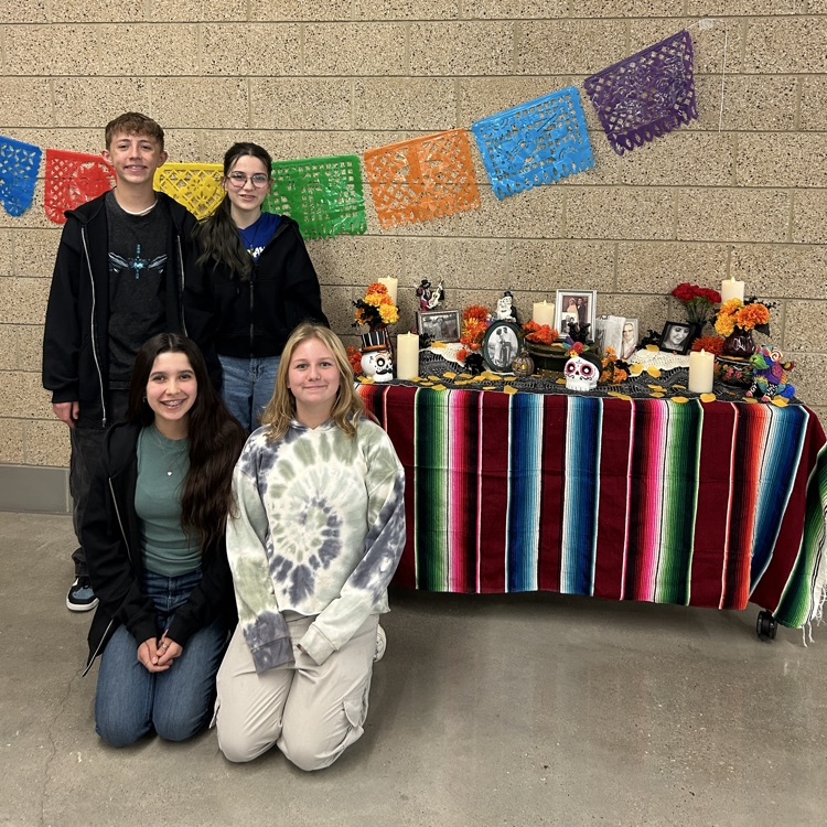 Four students stand next to an altar for Dia de los Muertos