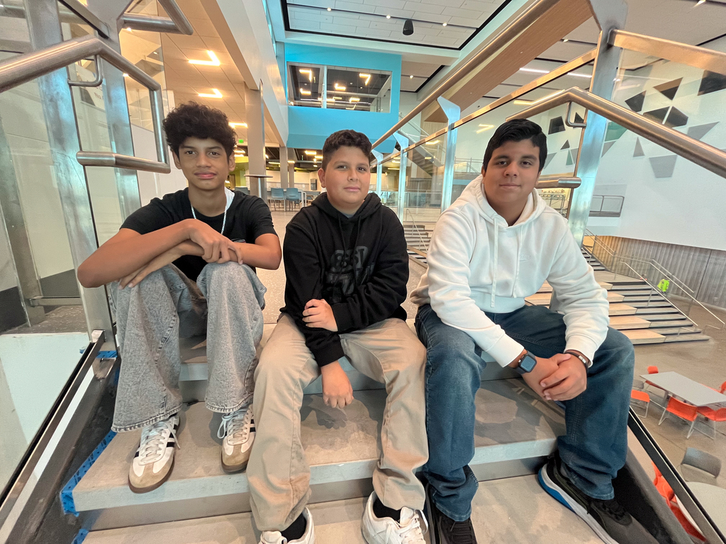 Three students smile while sitting on the stairs at school.