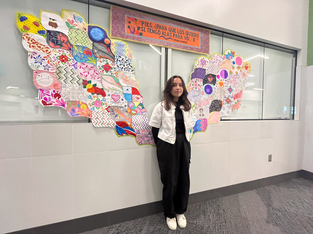 A student stands in front of an art piece that is wings.