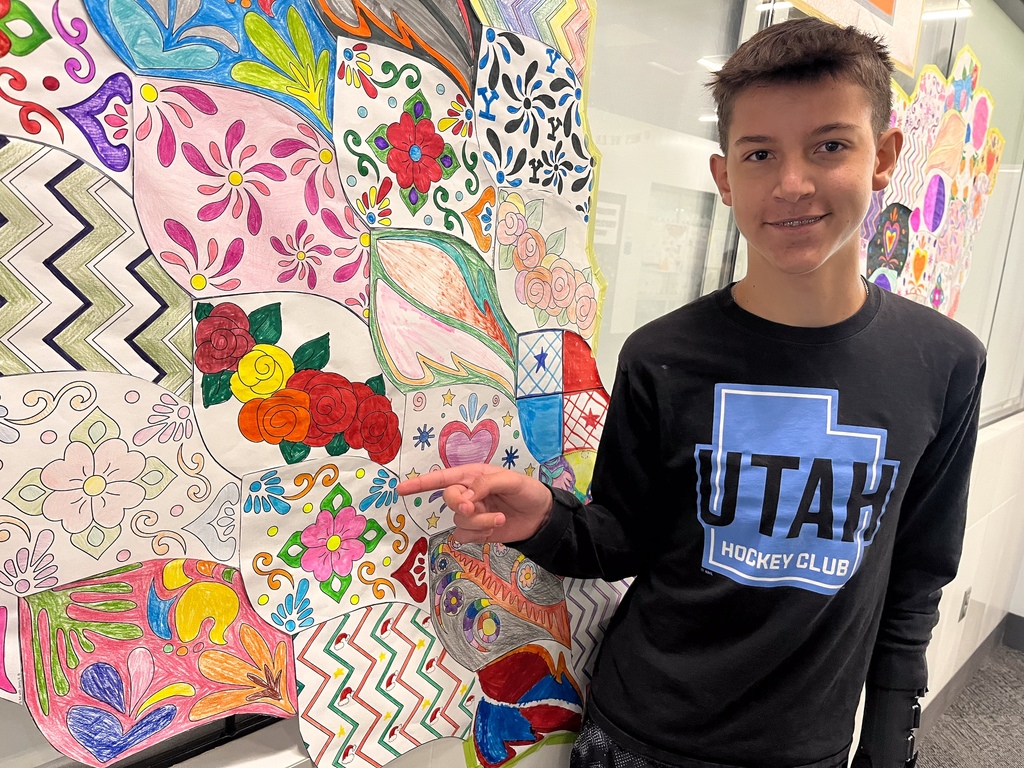 A student pointing to his artwork on the wall.