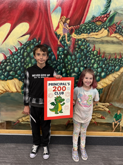 Two elementary-age students, a boy and a girl, stand in front of a colorful mural of a large green and red dragon. They are holding a bright red sign that reads "Principal's 200 Club" with a picture of a smaller green dragon and fireworks illustration. The boy is wearing a black hoodie and the girl is wearing a light-colored t-shirt.