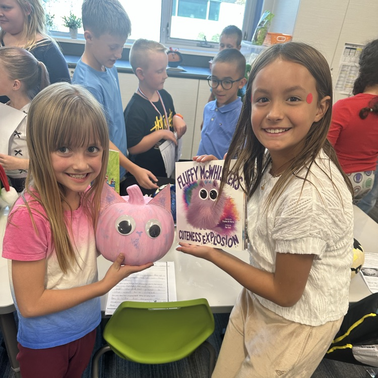 2 girls smiling, one holding a book fluffy mcwhiskers and another holding a pink pumpkin