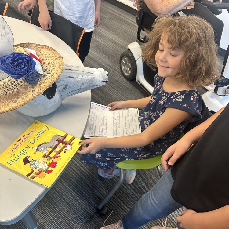 girl holds book the hungry donkey and paper smiling with a pumpkin decorated like a donkey