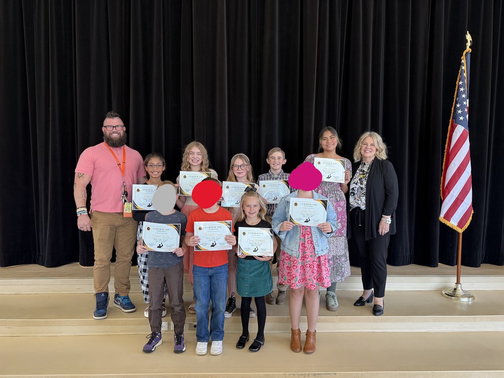 A group photo on a stage at Doxey Elementary. Nine students stand in the front row, each holding a certificate from the Martin Luther King Jr. Speech Contest. Two staff members, Principal Hansen and Mrs. Tweed, stand beside them. The background includes a black curtain and an American flag on a stand.