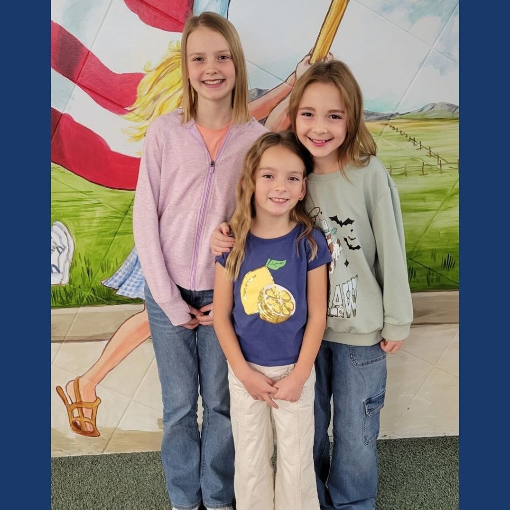 3 Girls posing for a picture in front of a wall with a painted American Flag.