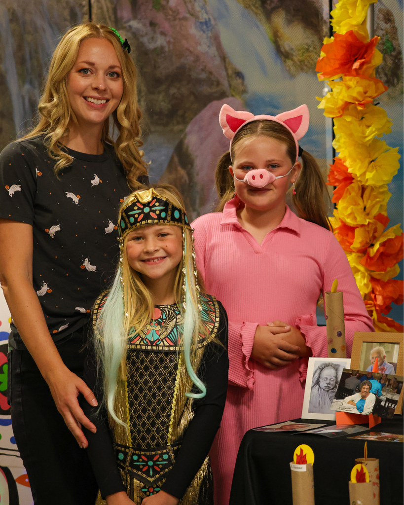 A parent and two students dressed up for halloween stand next to the ofrenda at Canyon Creek Elementary.