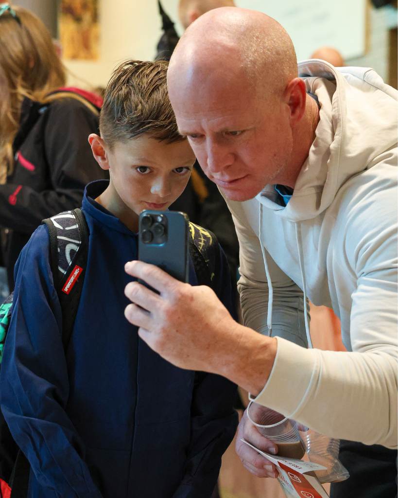A parent and student look at a phone while taking a photo of the ofrenda at Canyon Creek Elementary.