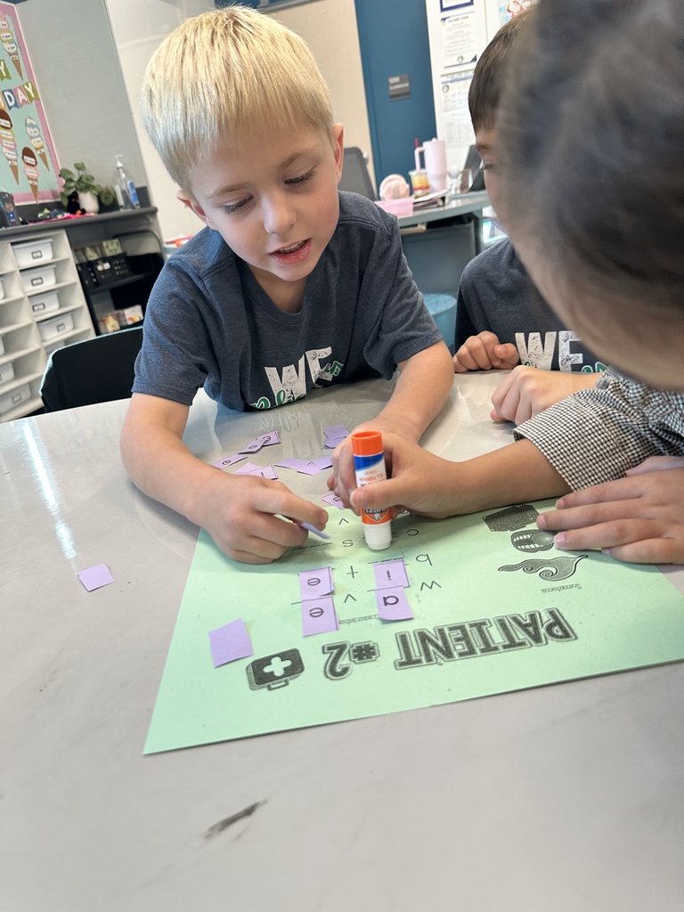 girl using a glue stick to paste a letter down while boys help