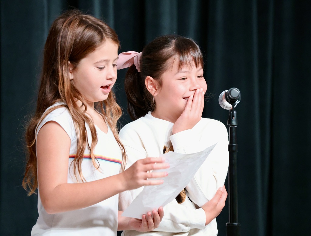 Students standing in front of a mic while reading a paper. 