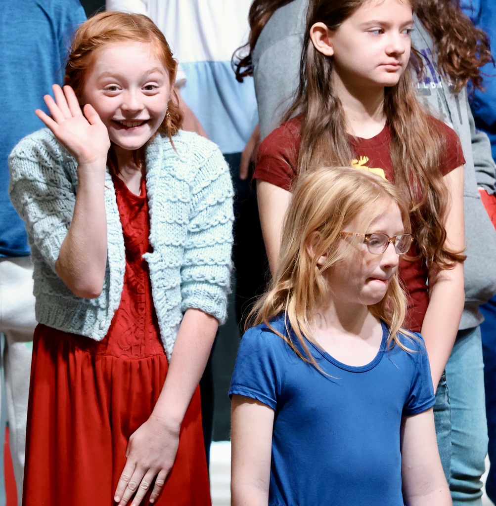 A student in a crowd smiling and waving her hand. 