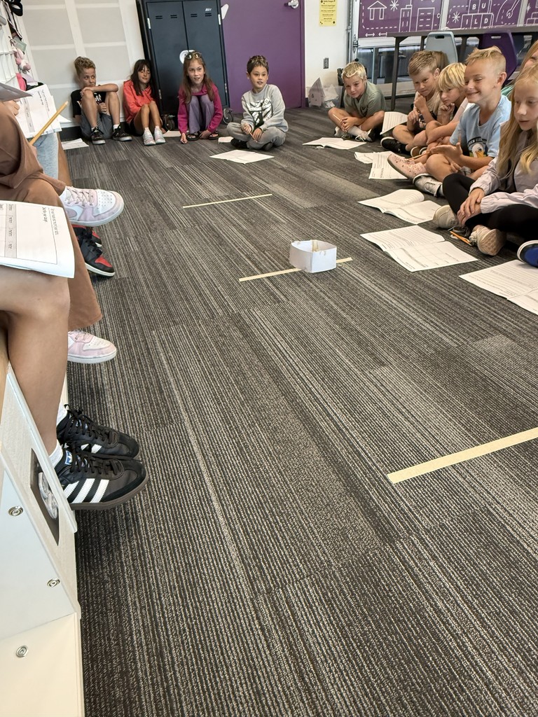 students sitting on the ground around a paper box