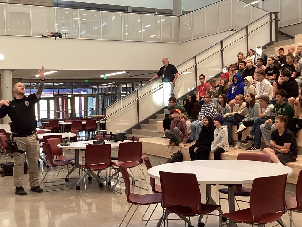 Police officer showing the drone to students sitting on the stairs.
