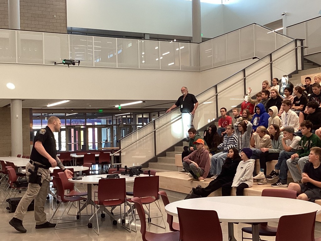 Police officer showing the drone to students sitting on the stairs.