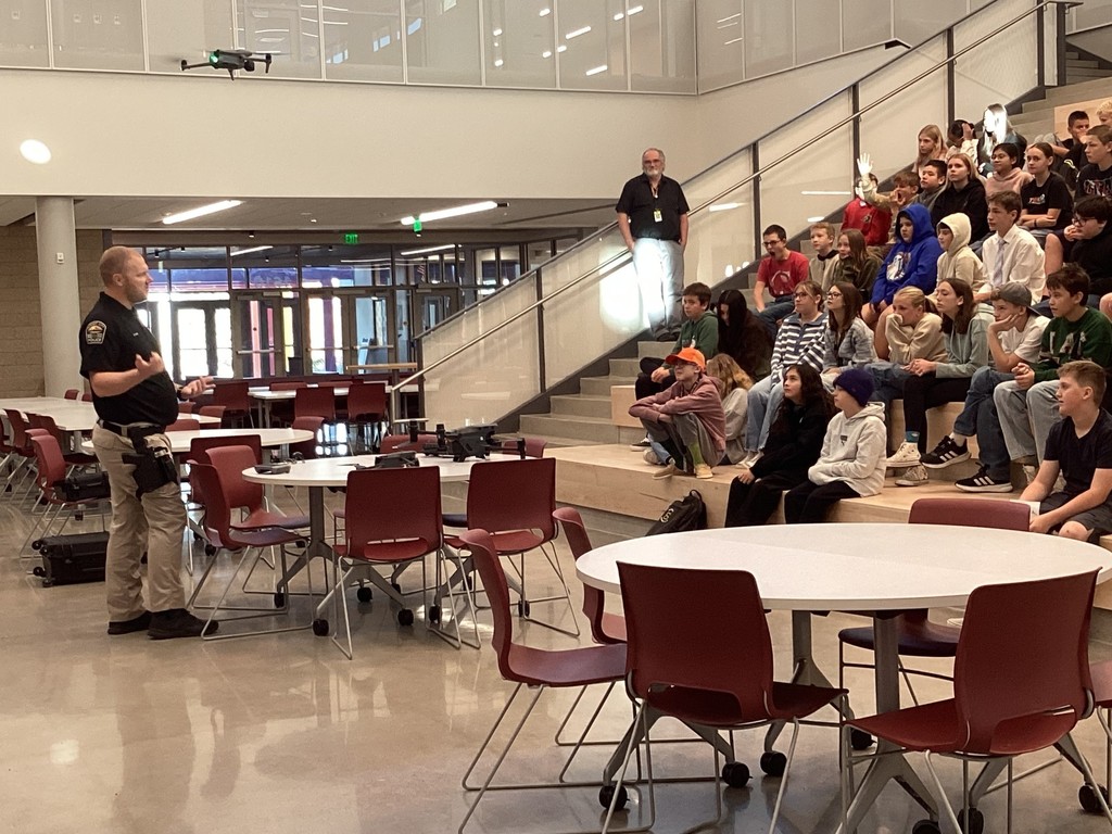 Police officer showing the drone to students sitting on the stairs.