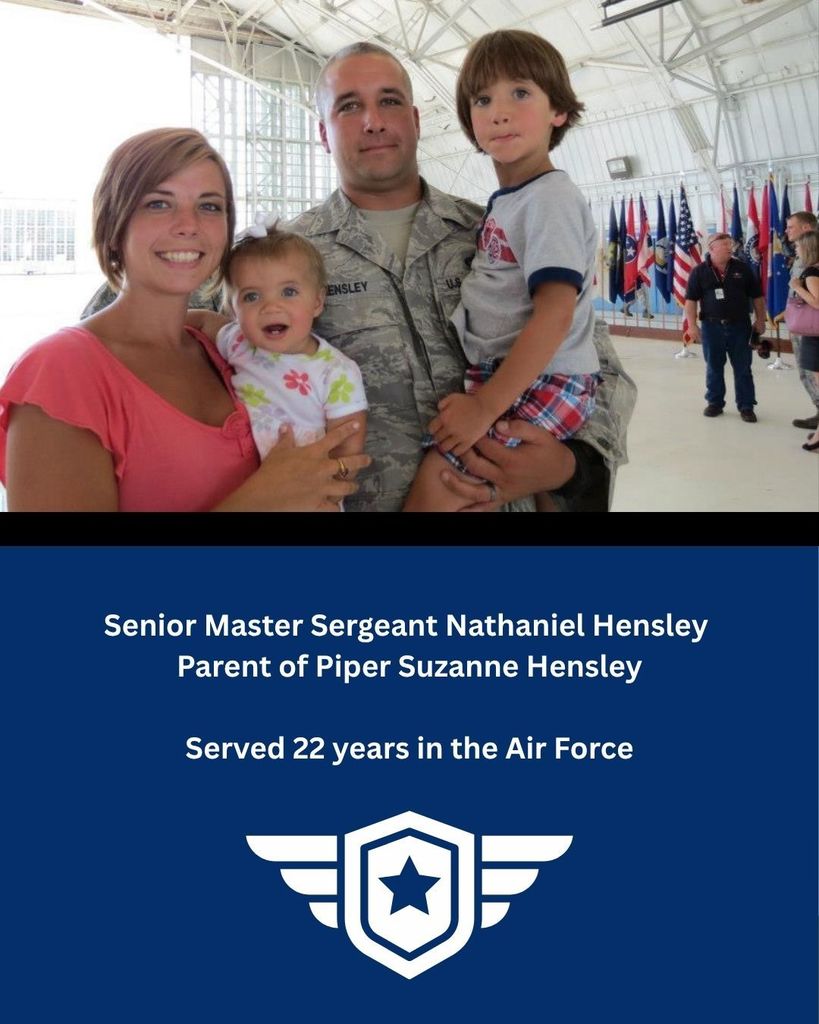 A mother and father holding two children standing in a airplane hanger. The man is in his military uniform.