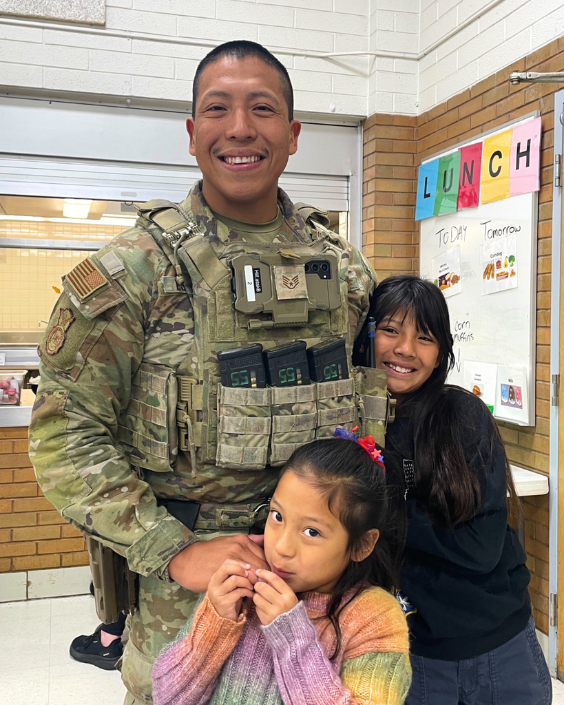 A military member standing with his children at school. 